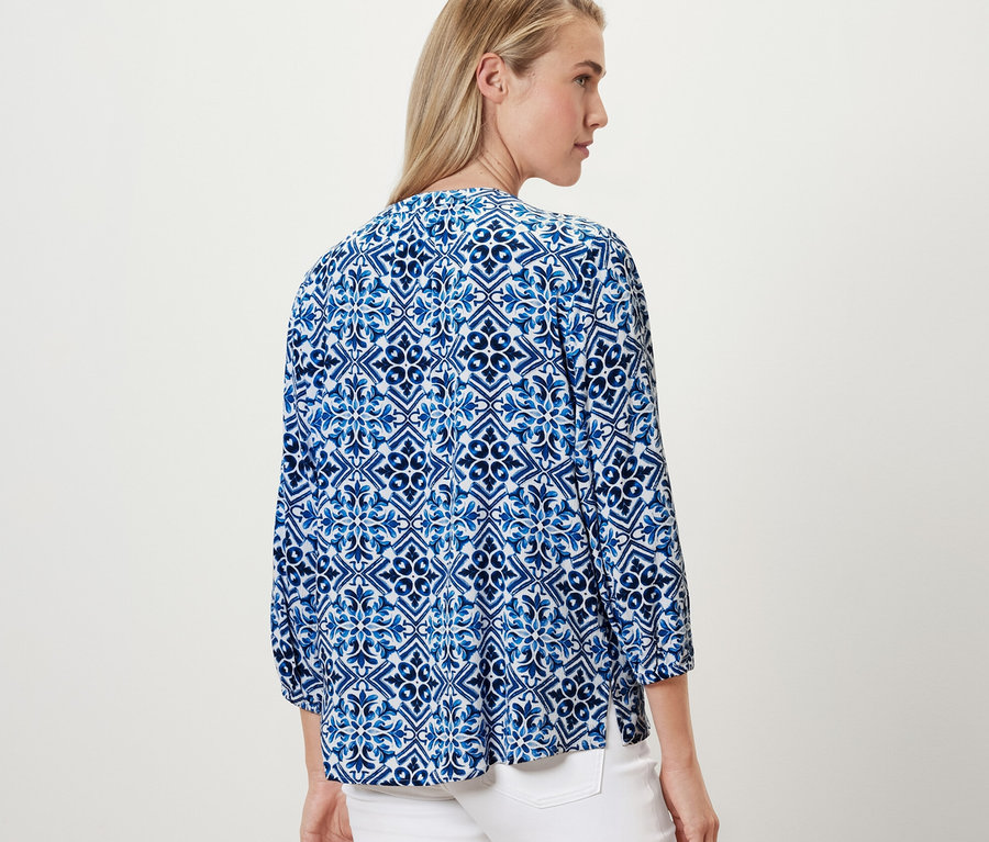 Frau trägt eine bedruckte Tunika-Bluse, blau.