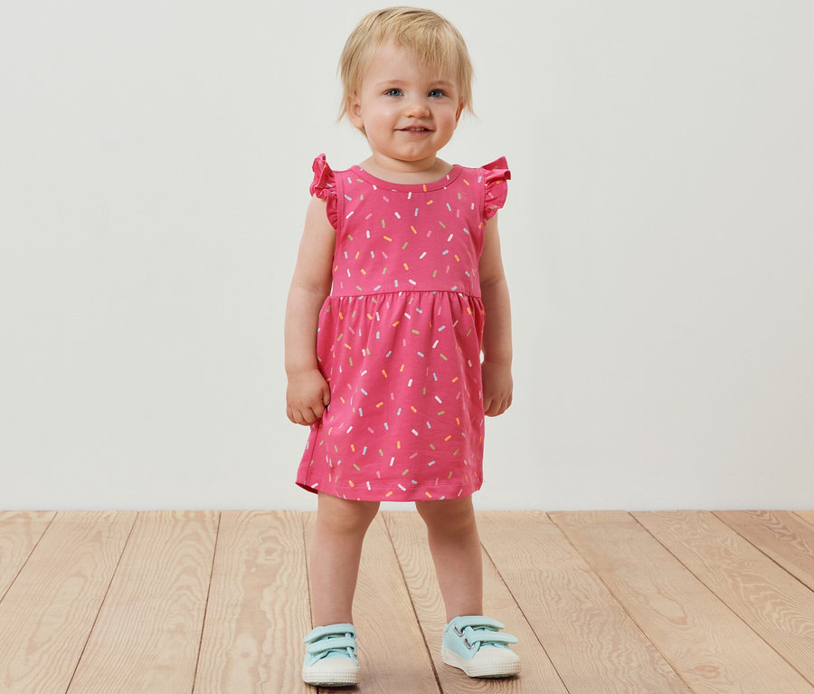 Lächelndes kleines Mädchen steht und trägt ein rosafarbenes Jerseykleid.