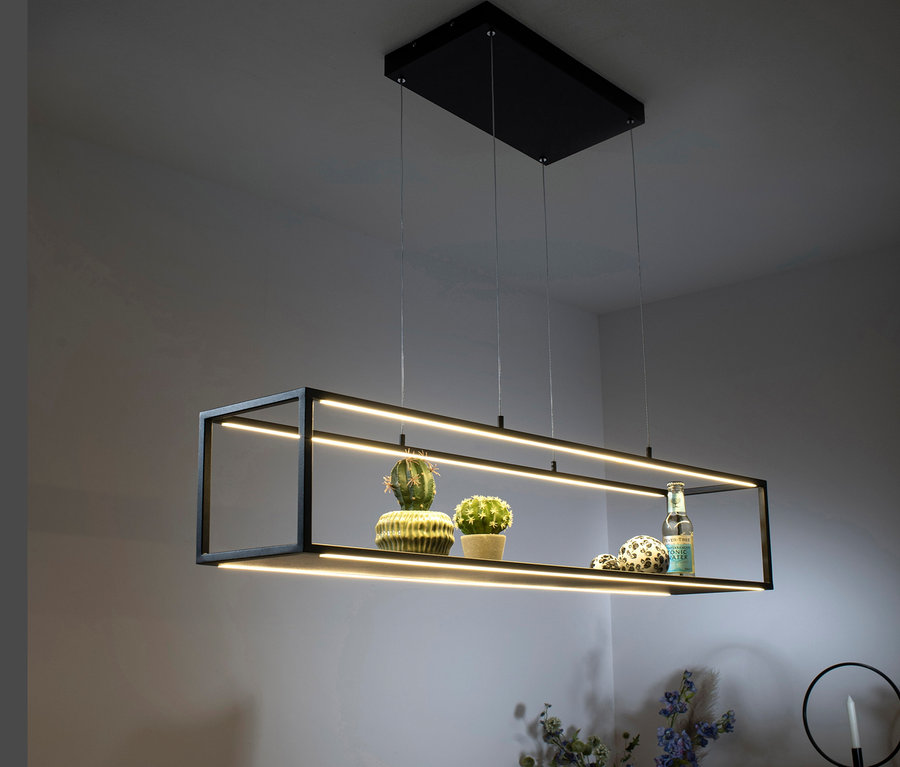 Eine schwarze LED-Pendelleuchte »Contura« hängt über einem Tisch, auf dem Dekorationen und Blumen stehen.