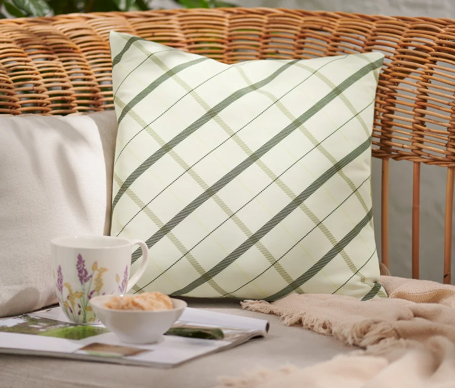 Auf einem Rattan-Sessel liegt ein Outdoor-Kissen mit Karomuster.