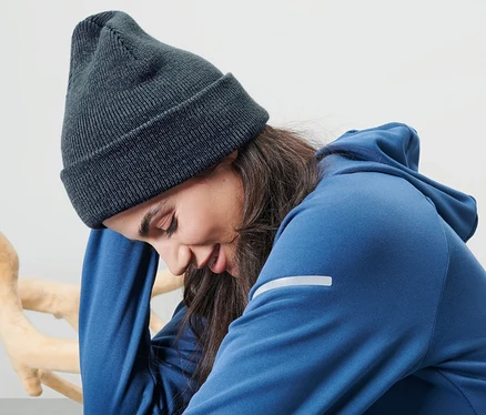 Frau sitzt und trägt eine blaue Strickmütze.