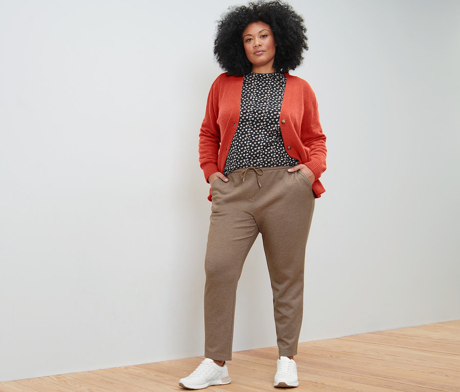 Frau posiert in beigen Joggpants, Langarmshirt mit Alloverprint und Cardigan mit V-Ausschnitt.