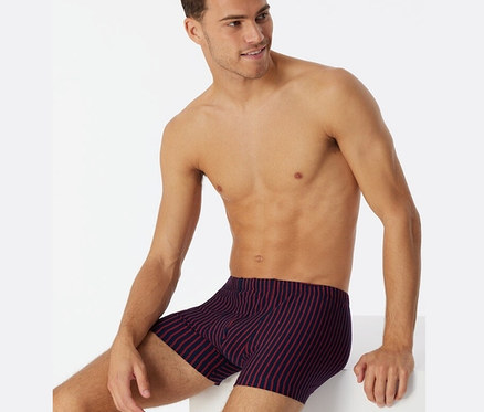 Mann sitzt und trägt rote SCHIESSER Shorts mit Bio-Baumwolle.