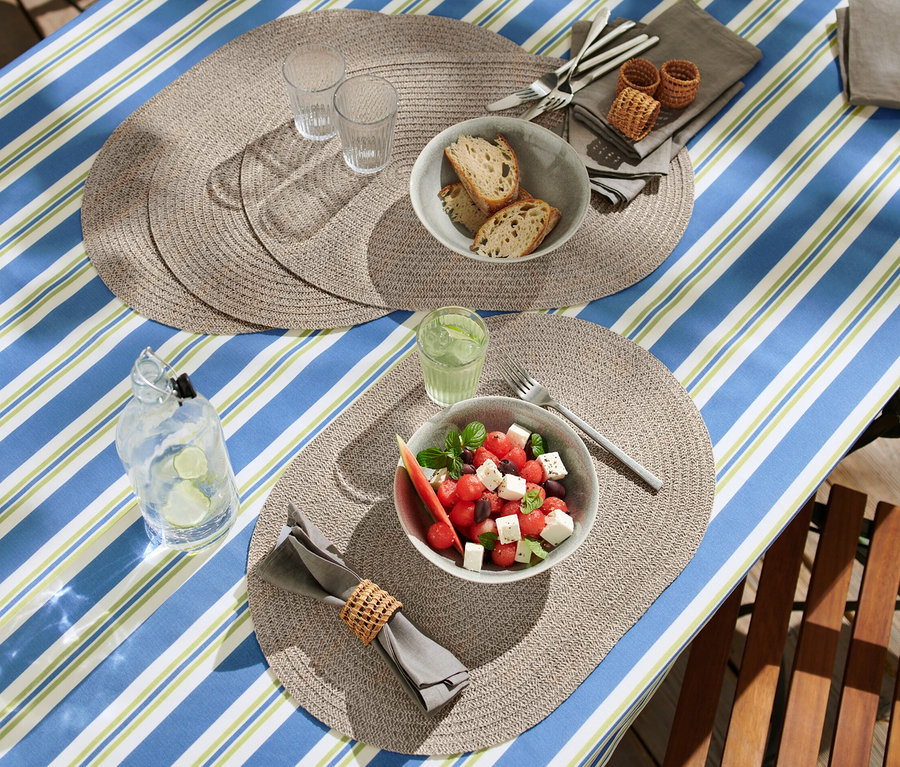 Gedeckter Tisch mit ovalen abwischbaren Platzsets, Salat, Brot und Getränken.