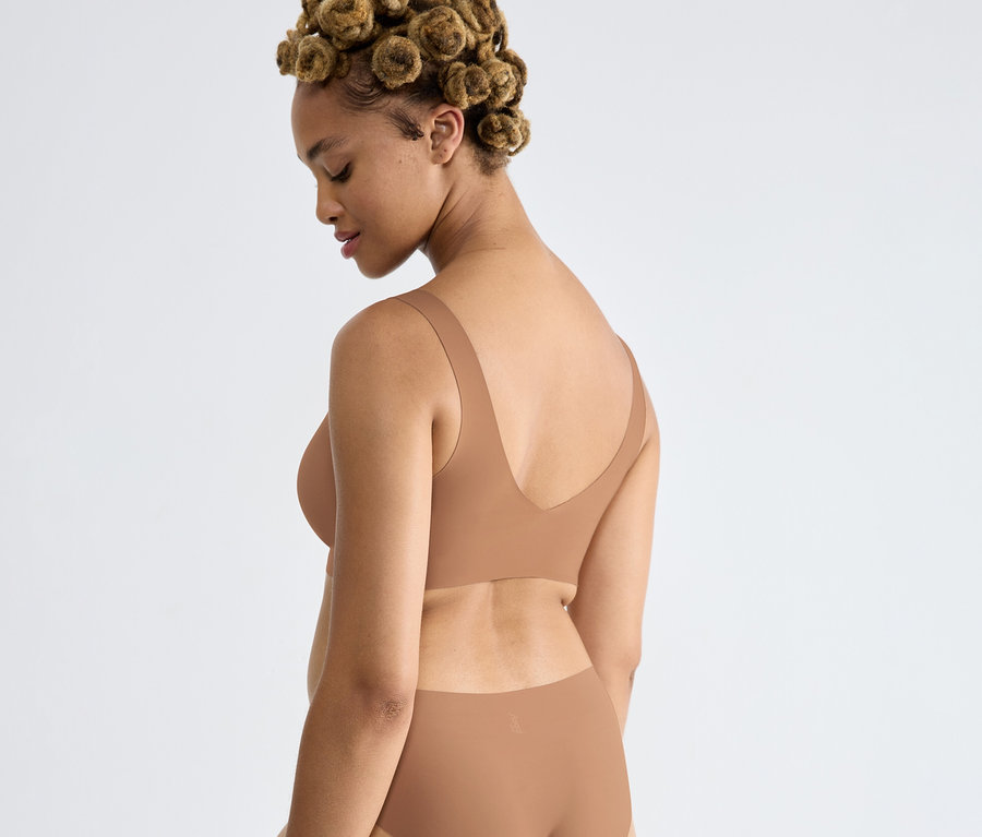 Frau trägt ein sloggi ZERO Feel 2.0 Bralette in Nostalgic Brown und passende Unterhose, blickt nach unten, Haare in kleinen Dutts.
