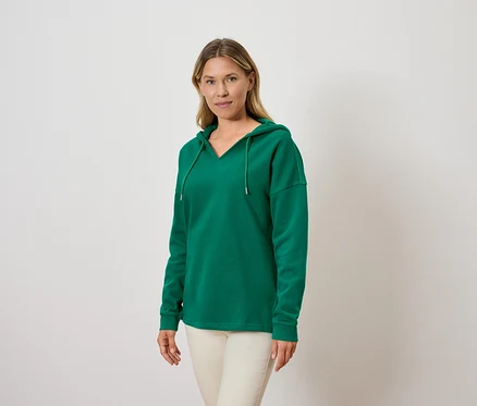 Frau trägt einen grünen Kapuzenpullover und helle Hosen.