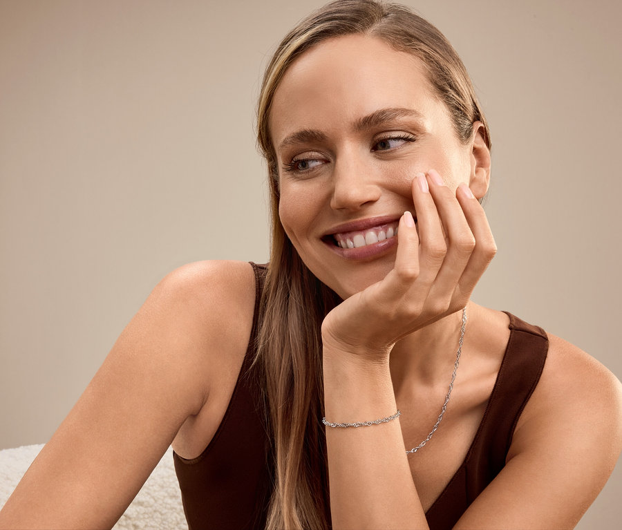 Lächelnde blonde Frau, die ihr Gesicht auf ihre Hand stützt, trägt ein Armband und eine Halskette.