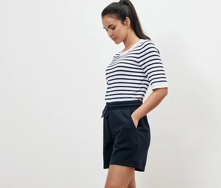 Frau mit gestreiftem T-Shirt und marineblauen Sweatshorts steht seitlich.
