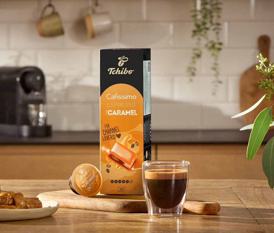 Espresso, Karamellbonbons und eine Packung Cafissimo Flavoured Edition – Espresso Caramel - 80 Kapseln auf einem Holztisch.