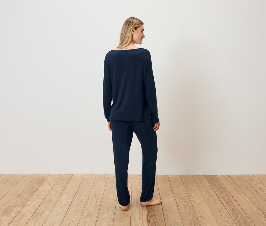 Frau in dunkelblauem Pyjama steht mit dem Rücken zur Kamera auf einem Holzboden.