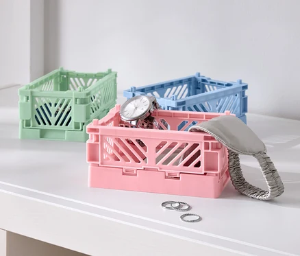 Drei farbige Faltboxen auf einem Tisch, eine rosa mit einer Uhr, eine blaue und eine grüne.