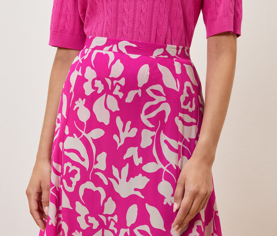 Eine Frau trägt ein pinkes Oberteil und einen Rock mit Blumenmuster.