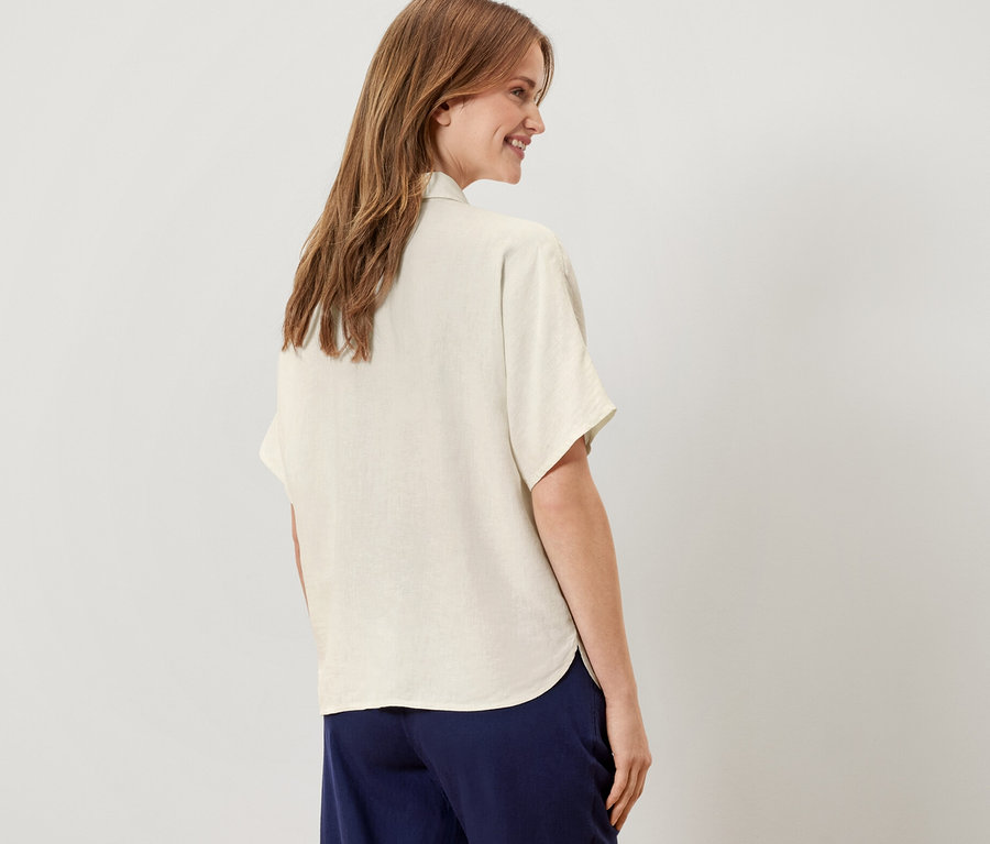 Frau steht mit dem Rücken zur Kamera und trägt eine cremeweiße Leinenbluse.