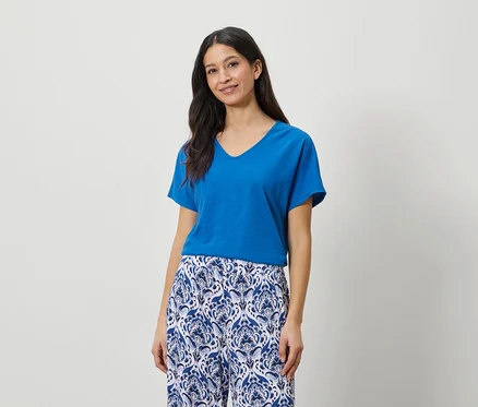 Frau trägt ein blaues T-Shirt und eine blau-weiß gemusterte Hose.