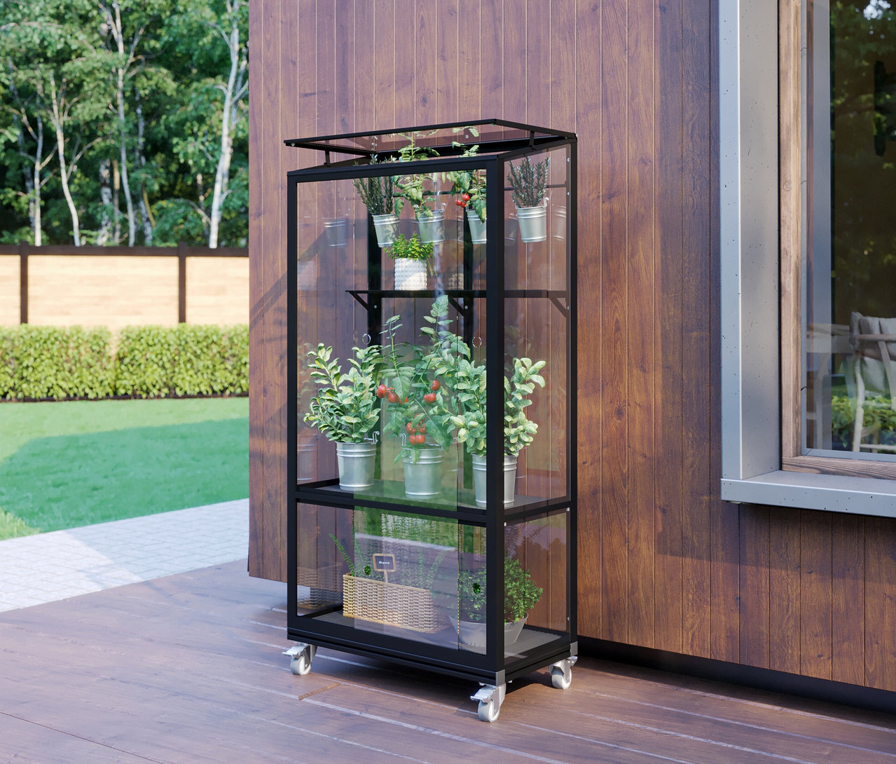 Das schwarze Vitavia Balkongewächshaus mit Rollfundament steht auf einer Holzterrasse und ist mit Pflanzen in Töpfen und einem Korb bepflanzt.