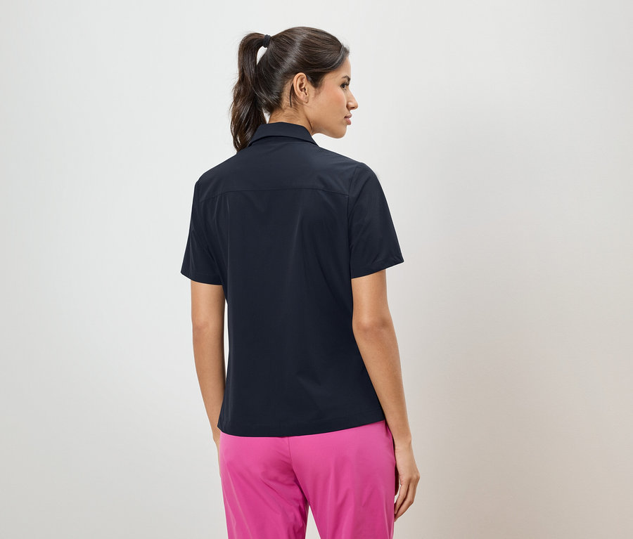 Rückansicht einer Frau mit Pferdeschwanz, die ein dunkelblaues Hemd und eine pinke Hose trägt.