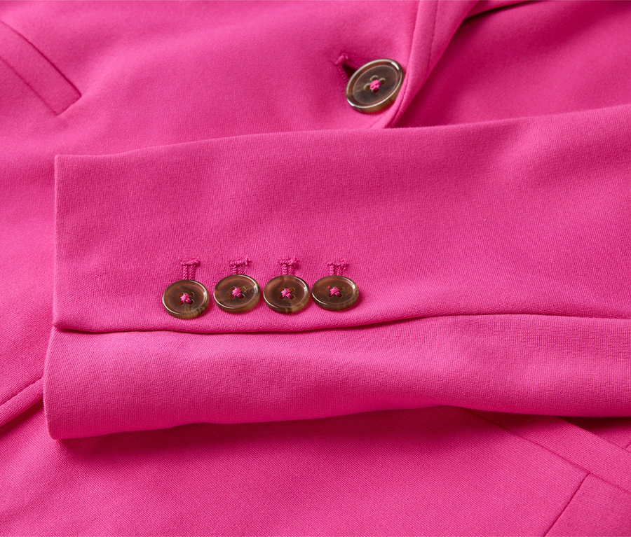 Nahaufnahme eines pinkfarbenen Blazerärmels mit vier Knöpfen am Ärmel und einem Knopf am Revers.