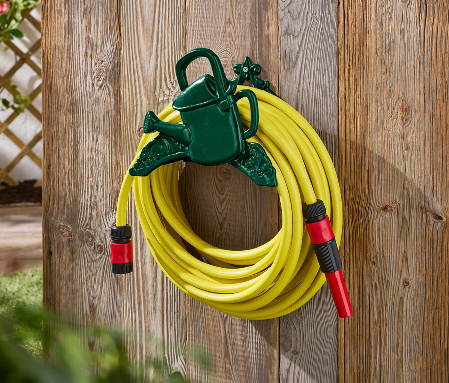 Ein gelber Gartenschlauch ist an einer grünen Halterung in Form einer Gießkanne an einer Holzwand befestigt.