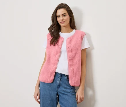 Frau trägt eine rosafarbene Teddy-Weste über einem weißen T-Shirt und blauen Jeans.