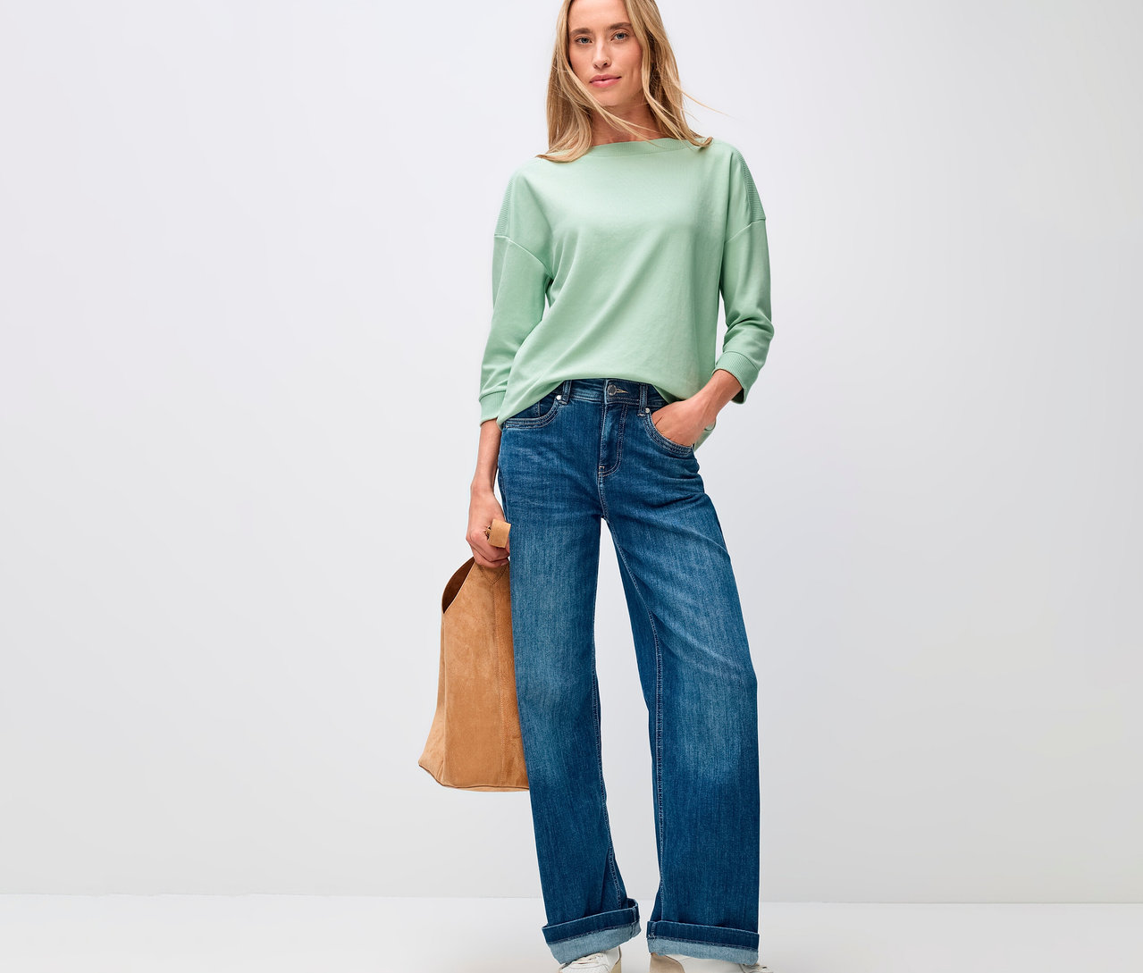 Frau in Jeans und einem Street One, T-Shirt mit Rippdetail in Salbeigrün, mit einer braunen Tasche.