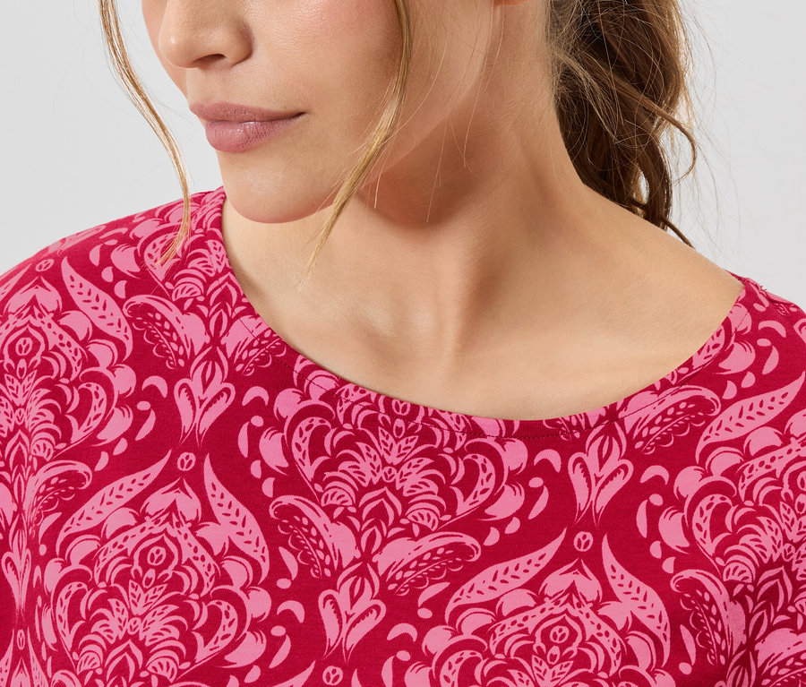 Nahaufnahme einer Frau, die ein rot-rosa gemustertes Oberteil trägt.