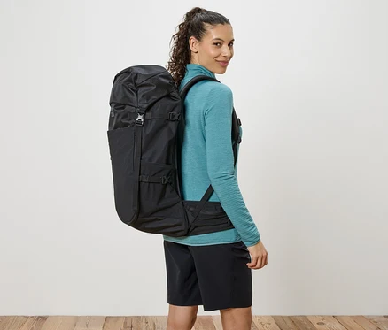 Frau mit einem schwarzen Rucksack, der über ihre Schultern hängt, und sie blickt über ihre Schulter.