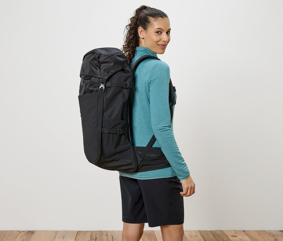 Frau mit einem schwarzen Rucksack, der über ihre Schultern hängt, und sie blickt über ihre Schulter.