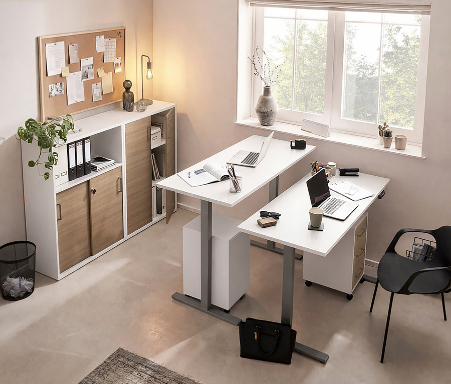 Büroraum mit zwei weißen Schreibtischen, Laptops, Büromaterial und einem Schrank mit Schiebetüren unter einer Pinnwand.