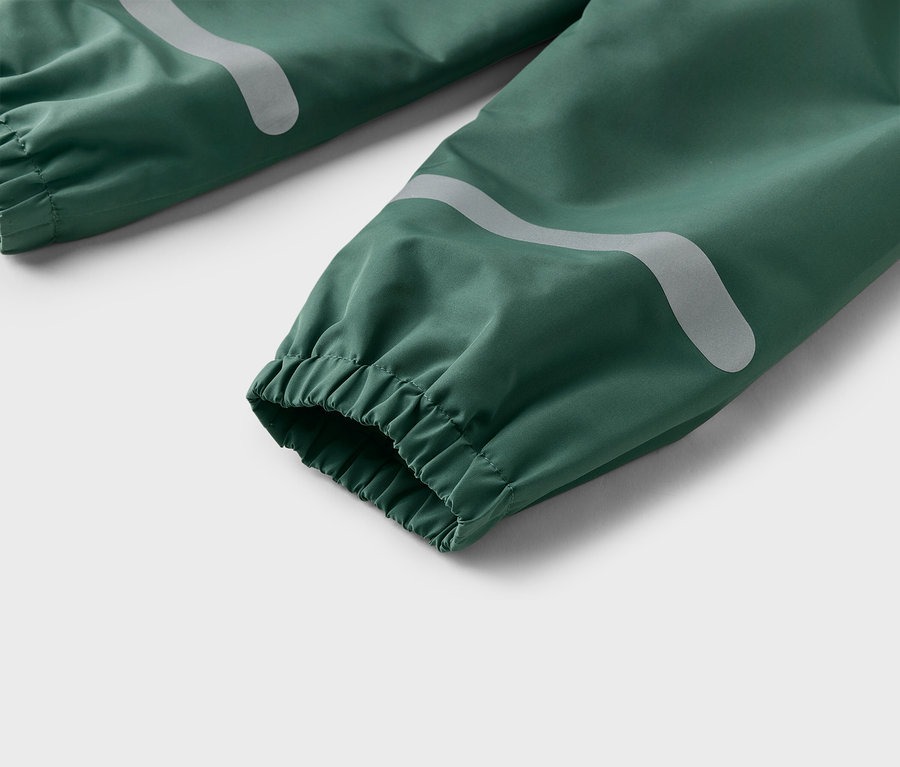 Nahaufnahme von grünen Regenhosen mit elastischen Bündchen und reflektierenden Streifen.