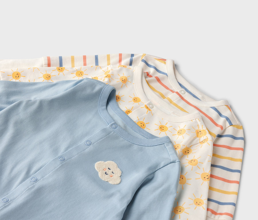 Nahaufnahme von drei Baby-Overalls: einfarbig hellblau mit Wolkenapplikation, weiß mit Sonnen und gestreift.