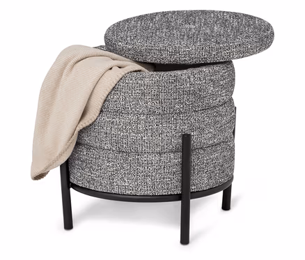 Ein grauer, runder Hocker mit schwarzem Beingestell und einer beigen Decke darauf.