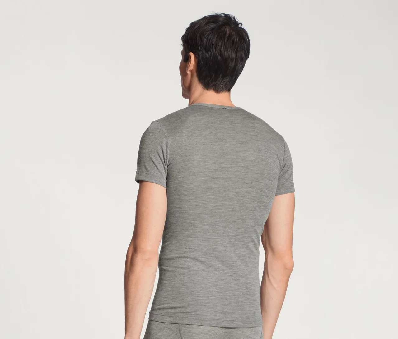 Mann von hinten in einem grauen Kurzarm-T-Shirt und passender Unterwäsche vor weißem Hintergrund.