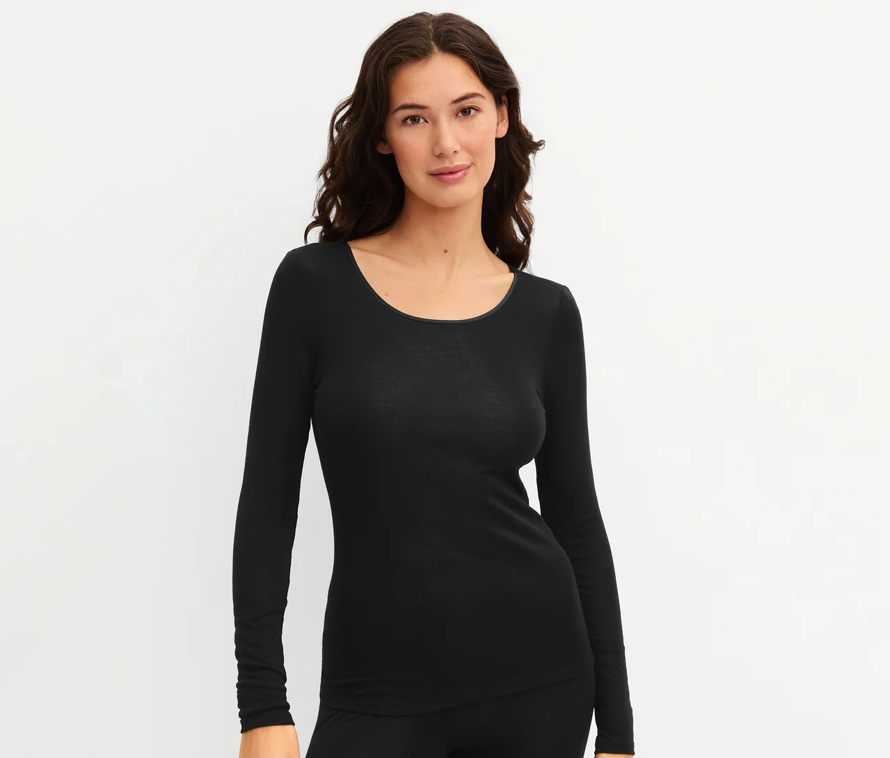 Frau trägt ein schwarzes CALIDA »True Confidence« Langarm-Shirt und eine schwarze Hose, blickt in die Kamera und lächelt.