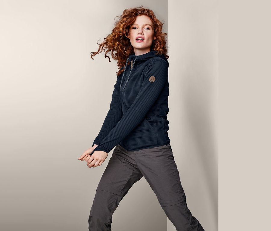 Rothaarige Frau posiert in marineblauer Kapuzenjacke.