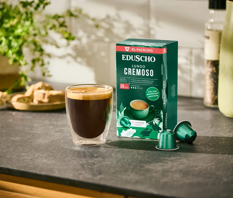 Ein Glas Kaffee steht neben einer Packung EDUSCHO Lungo Cremoso - 20 Kapseln.