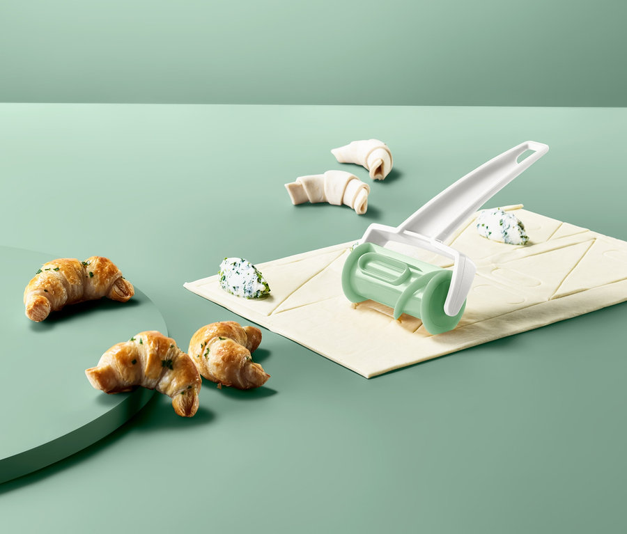 Croissant-Roller liegt auf Teigblatt mit Füllung, neben gebackenen Croissants.