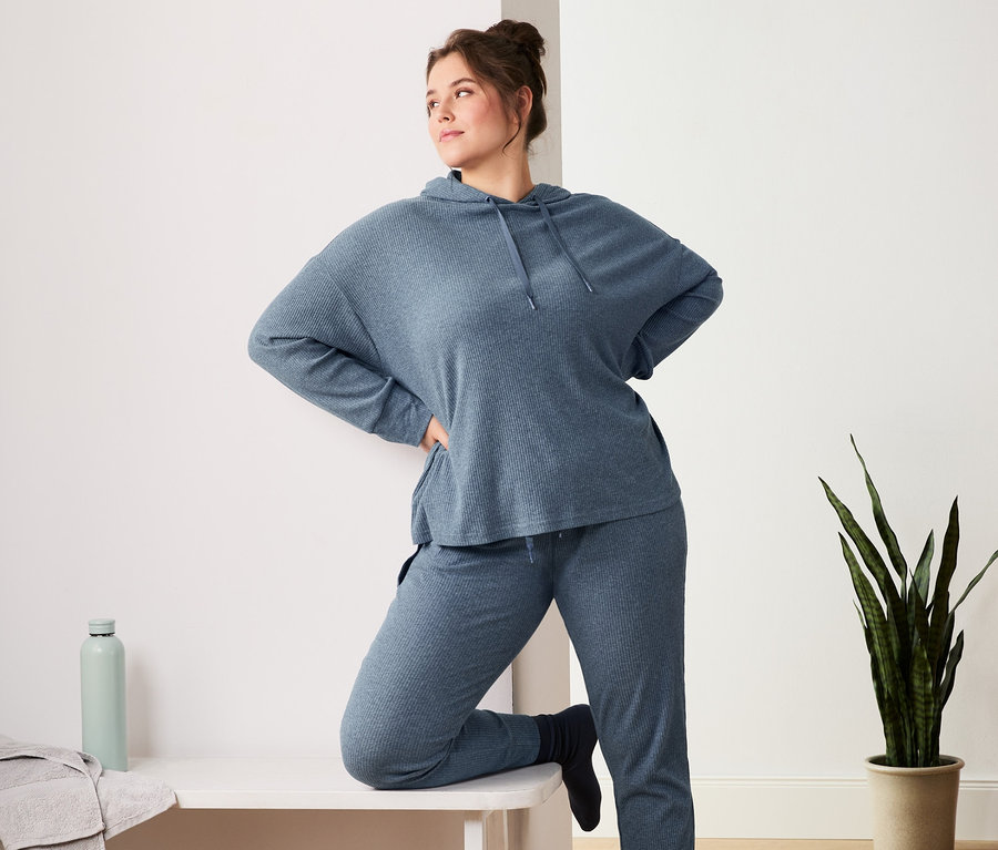 Frau posiert in blauer Relaxhose und Relaxshirt. Auf der Bank liegen 2 Paar Ripp-Socken.