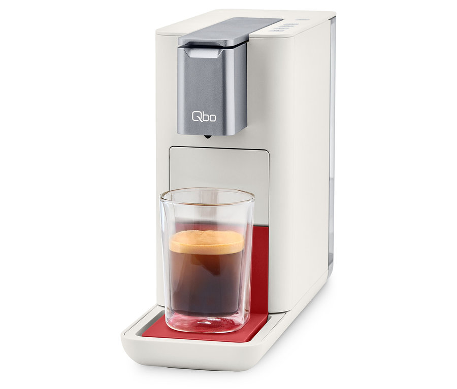 Qbo ESSENTIAL Bright Coral Kaffeemaschine mit einer Tasse Kaffee.