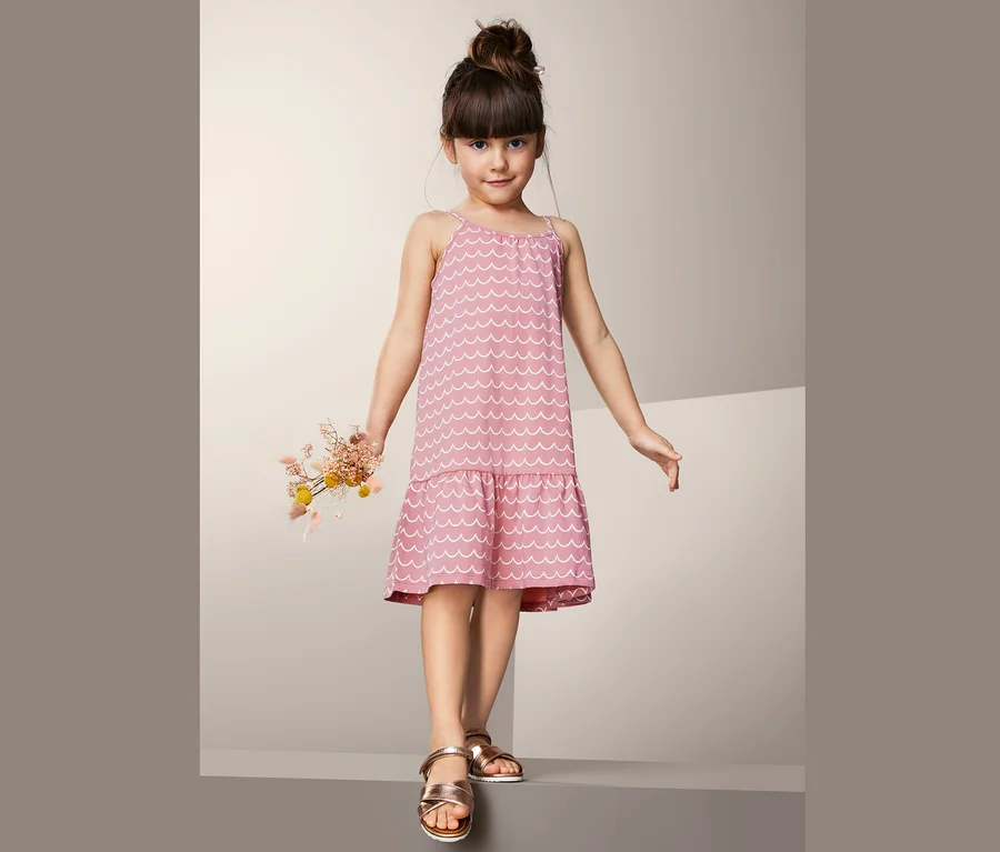 Ein Mädchen trägt ein rosa Jerseykleid mit weißem Wellenmuster und hält einen Strauß Trockenblumen.