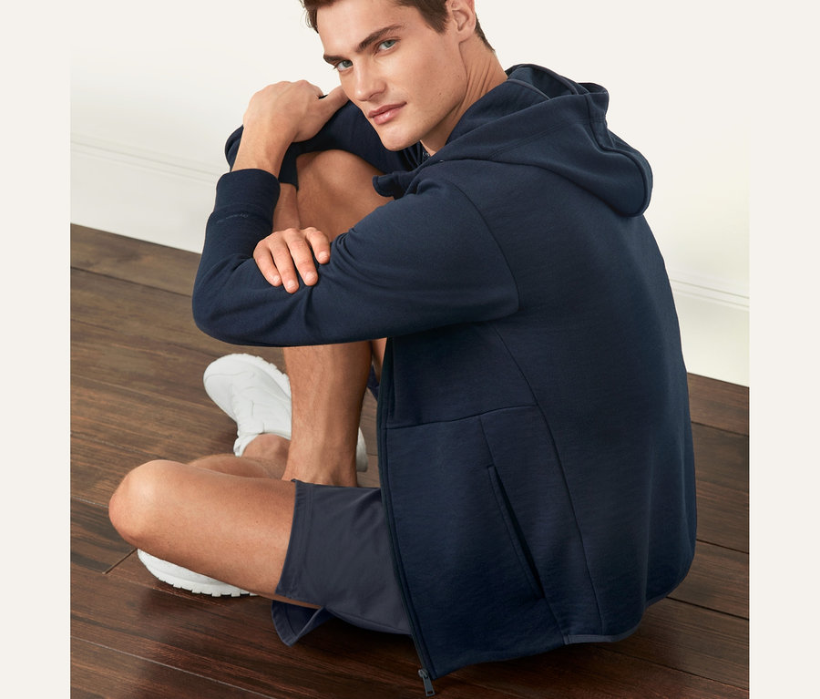 Ein Mann sitzt in einer dunkelblauen Funktionssweatjacke auf dem Boden.