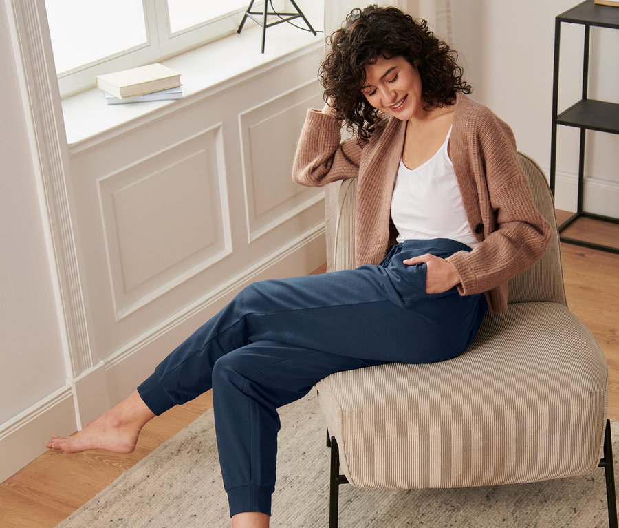 Frau sitzt auf einem Stuhl und trägt eine Loungewear-Hose.