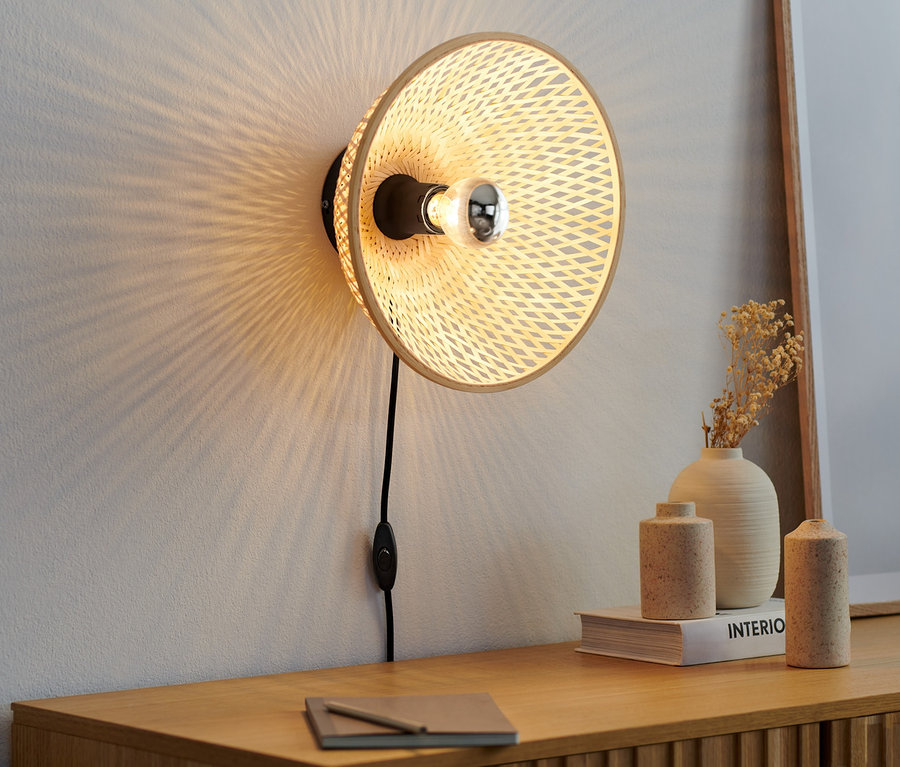 Wandleuchte mit Bambusschirm hängt an der Wand über einer Holzkommode.