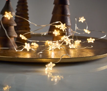 LED-Microlichterkette, Sterne, liegt auf einem goldenen Tablett neben hölzernen Zierbäumen.