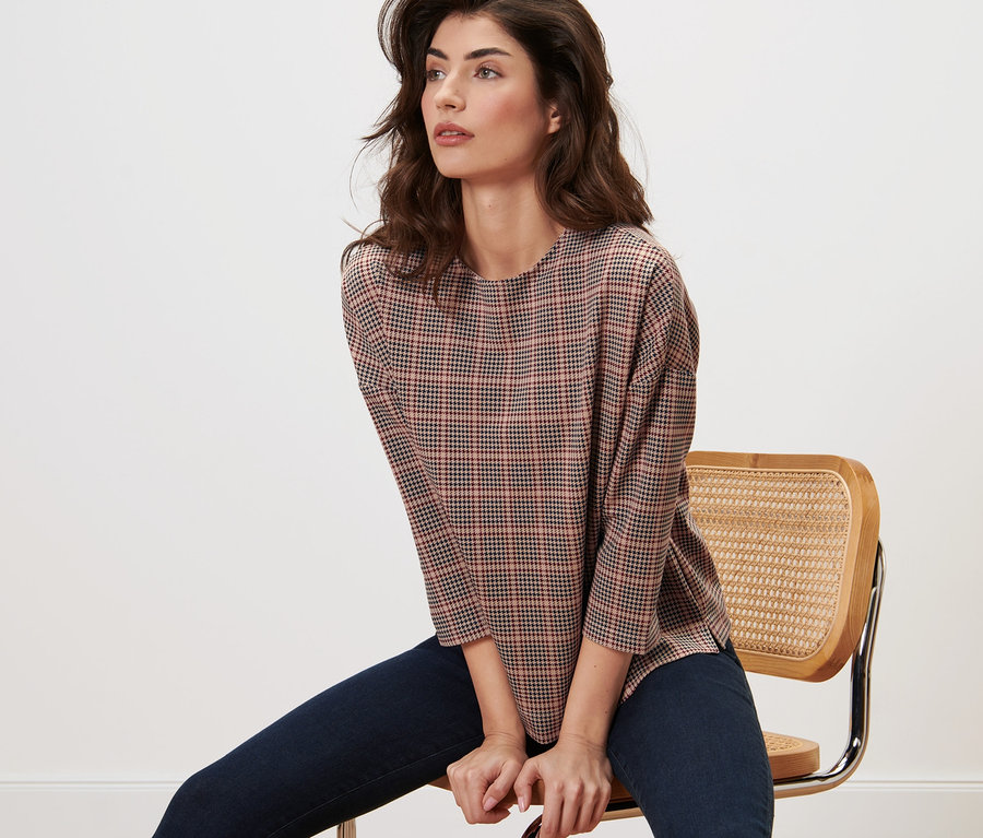 Frau sitzt auf Stuhl und trägt Sweatshirt mit 3/4-Arm, Hahnentritt.