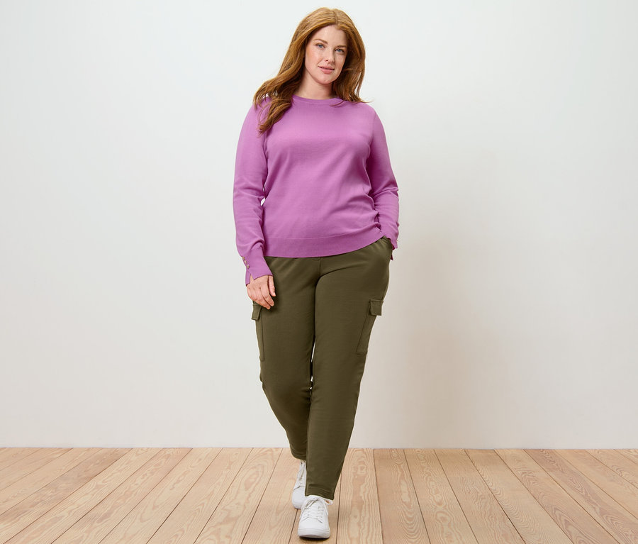Frau posiert in Feinstrickpullover und khaki Joggpants mit Cargo-Taschen.
