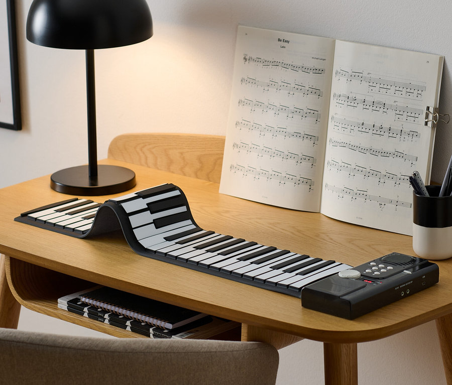 Auf einem Tisch liegen ein elektronisches Rollpiano, Noten und eine Lampe.