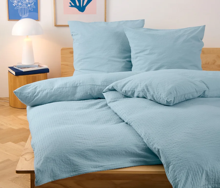 Hellblaue Seersucker-Bettwäsche in Normalgröße und Übergröße auf einem Bett.