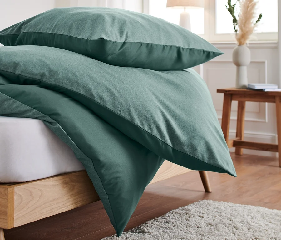 Stapel grüne Microfaser-Flanell-Bettwäsche liegt auf einem Bett neben einem beigen Teppich.