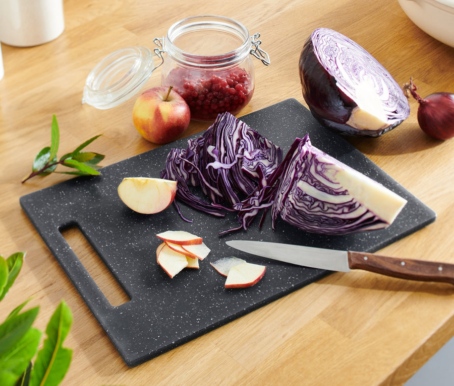 Geschnittenes Rotkraut und Äpfel auf einem Schneidebrett in Granitoptik mit Messer.