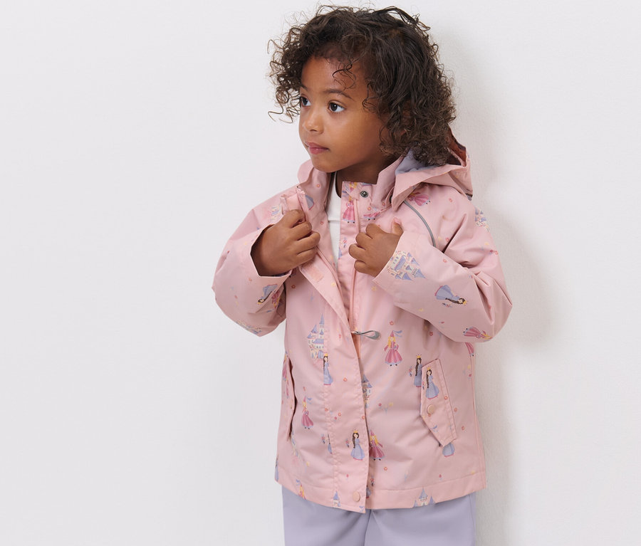 Mädchen schliesst eine Kinder-Regenjacke mit Prinzessinnenmuster.